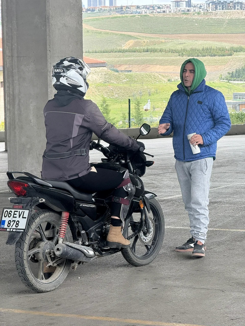 A helmeted rider talking to a person beside the motorcycle in the training area