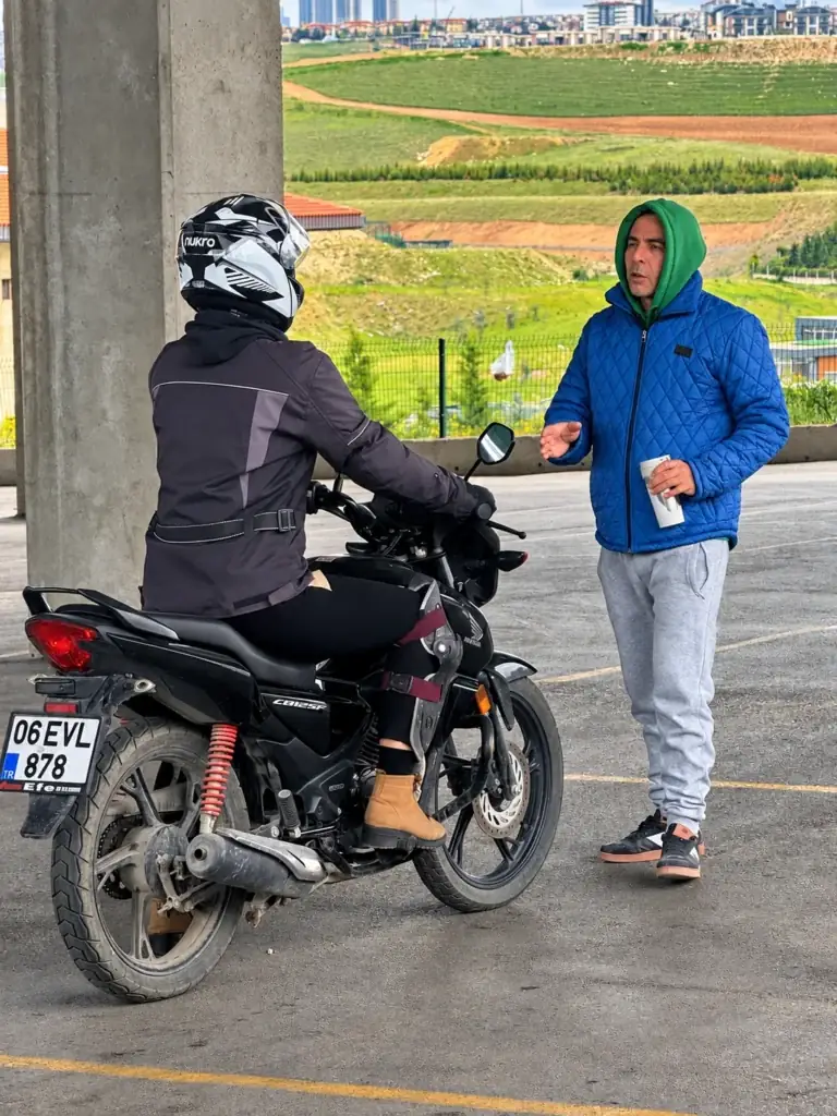 Helmeted rider on a black motorcycle talking to a person in a blue jacket