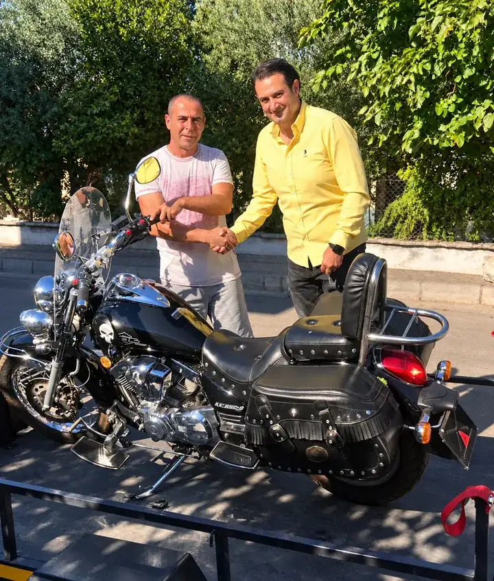 Römork üzerindeki motosikletin yanında tokalaşan iki kişi